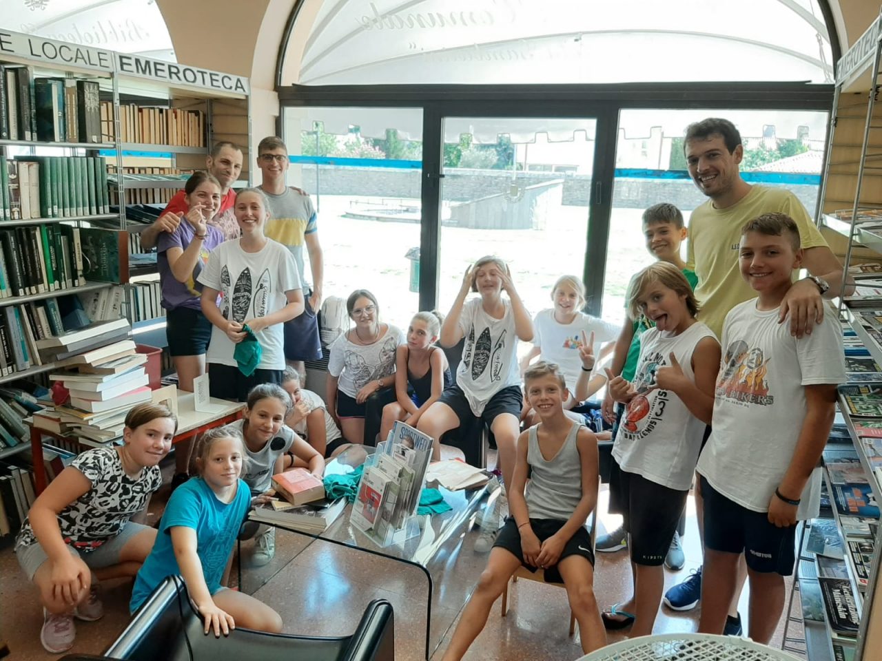 Ragazzi ripuliscono gli scaffali della biblioteca, armati di strofinacci
